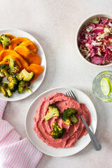 A healthy breakfast with beet hummus, baked sweet potato, and broccoli, topped with a fresh radish and cabbage salad, offering protein and nutrients