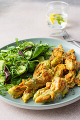 Fried zucchini flowers in batter and mix salad with cucumbers close up
