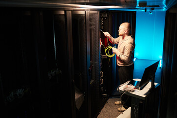 IT technician managing network cables in a high-tech data center with advanced servers and equipment surrounding him