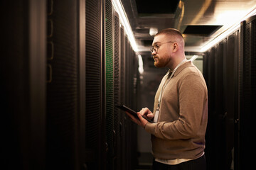 Fototapeta na wymiar Individual monitoring servers in modern data center holding tablet in hand. Wearing glasses and observing various indicators on server racks