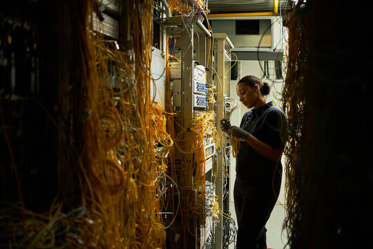 Technician checking server racks and organizing network cables in server room with focus on managing and maintaining technology infrastructure