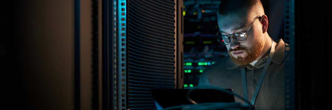 Young technician focusing on server maintenance in well-lit data center. Surrounded by networking equipment, performing checks on servers, concentrating intensely on task
