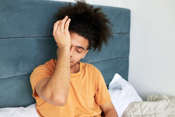 Indoor image of tired black sleep-deprived guy of 20s with afro hairstyle trying to wake up from night sleep rubbing his eyes to get up and start highly productive day after going to bed late