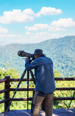 Man, photographer is wearing hat taking photos with Dslr camera and telephoto lens in green forest at Khao Yai's 30th km Viewpoint in the Khao Yai National Park, Thailand.Vertical.
