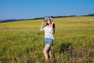 Woman in summer hat with brim walking in rural field in summer by road