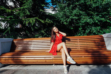 Brunette in a red polka dot dress in summer sitting on a bench