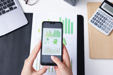 Woman taking photo of document using scanning app on smartphone at desk in office, above view