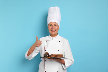 Professional pastry chef with desserts showing thumbs up on light blue background