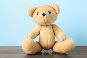 Cute teddy bear on wooden table against light blue background