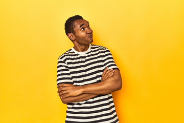 African American man in striped t-shirt, yellow studio, dreaming of achieving goals and purposes