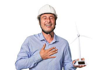 A middle-aged architect man holding a windmill model laughs out loudly keeping hand on chest.