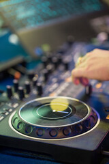 A detailed close-up shot of a DJ's hand operating a turntable, capturing the essence of a live DJ performance. The image highlights the turntable's jog wheel, knobs, and faders, with a blurred backgro