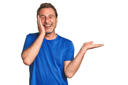 A middle-aged man isolated holds copy space on a palm, keep hand over cheek. Amazed and delighted.