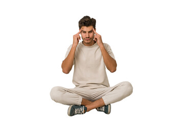 Young caucasian man sitting on the floor isolated on white background touching temples and having...