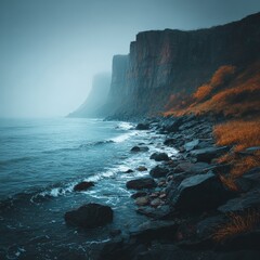 Obraz premium Misty Coastline: Rocky Cliffs Meet the Sea in Dramatic Scenery with Autumnal Hues in the Overcast Conditions 