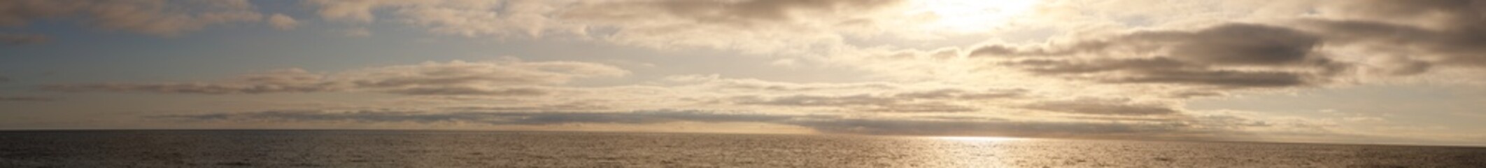 A blurry photo of a beach with a cloudy sky and a sun in the background