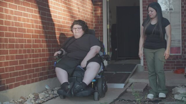 Muscular Dystrophy adolecsent in wheelchair going down ramp monitored by mom