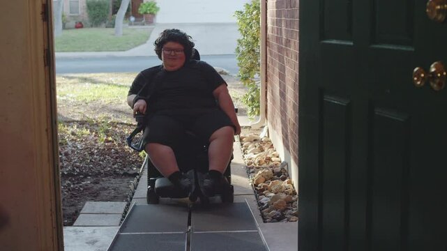 Muscular Dystrophy adolecsent in wheelchair approaches handicap ramp into house