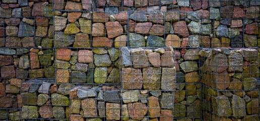 Gabion wall, decorative grass in urban design. Retaining wall made of large stones in metal.