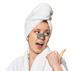 Young Caucasian redhead with pore strip points with thumb finger away, laughing and carefree.