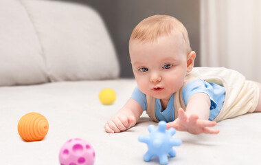 six month old baby reaches for toys while lying on tummy