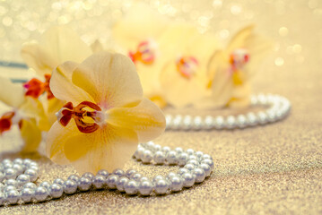 yellow Orchid and pearl necklace on a shiny gold background
