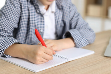 Little boy doing homework at wooden table indoors, closeup