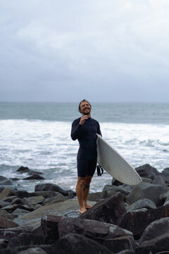 Man holding surfboard while standing on rock on beach
