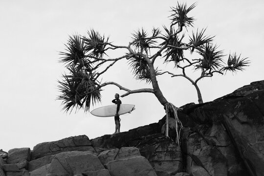 Side view of man with surfboard standing by rock