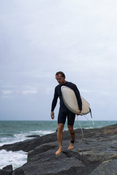 Side view of man with surfboard standing by rock
