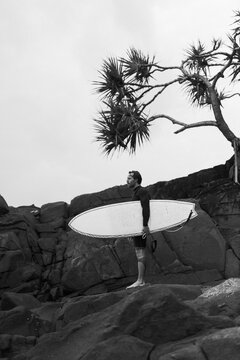 Man with surfboard standing on rock against cloudy sky