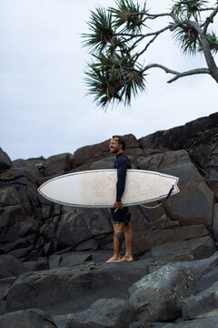Man holding surfboard while standing on rock on beach