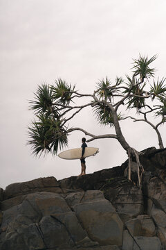 Man with surfboard looking away while standing on rock