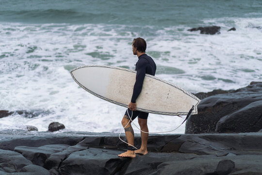 Side view of man with surfboard standing by rock