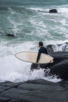 Side view of man with surfboard standing by rock