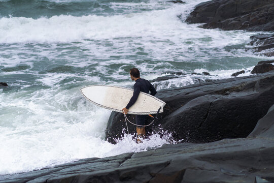 Man with surfboard looking away while standing on rock