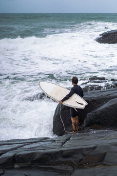 Male surfer in between rocks before jumping in the water to go surfing