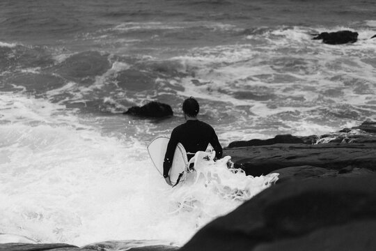 Male surfer in between rocks before jumping in the water to go surfing