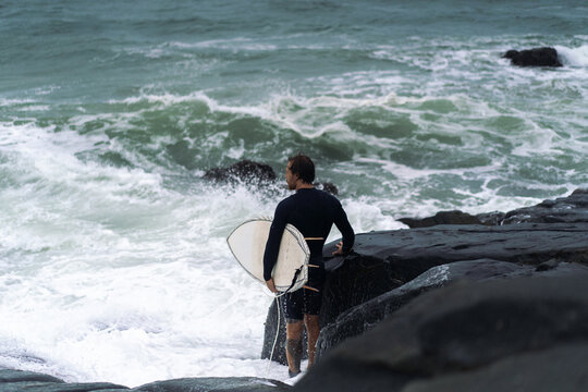 Man with surfboard looking away while standing on rock