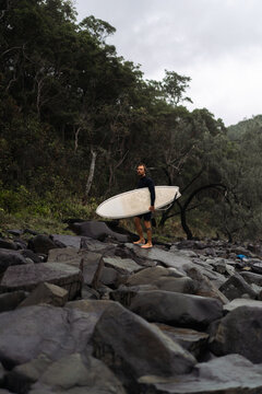 Man carrying surfboard while walking on rock