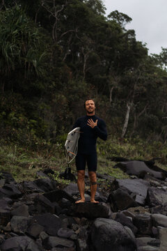 Man carrying surfboard while walking on rock