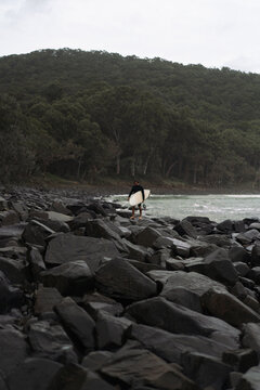 Man carrying surfboard while walking on rock