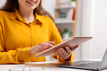 Fototapeta premium Woman using modern tablet at desk indoors, closeup. Space for text