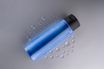 Face hyaluronic toner or essence in blue bottle on gray background with drops of water. Unbraiding packaging presentation. Mockup for designers