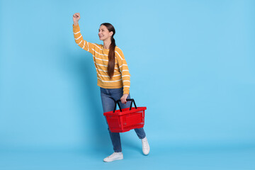 Smiling woman with shopping basket on light blue background