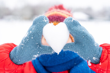 Snowy day joy as child shapes heart from snow in winter landscape wearing colorful attire