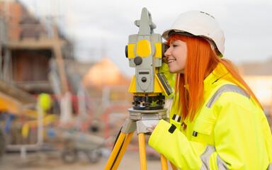 Portrait of Female Surveying expert in bright hi-viz safety coat operating surveying instrument to...