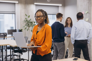 African american woman using laptop, professional team collaborating, diverse colleagues brainstorming in sleek workspace, sharing insights during strategic meeting