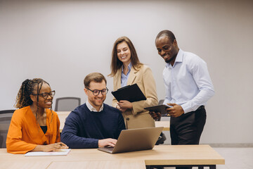 Four business colleagues collaborating on a project, using laptop and analyzing data in a modern office environment