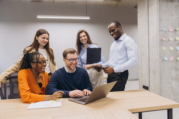 Fototapeta premium Professional team collaborating on laptop, diverse colleagues working together in modern office setting, sharing ideas and innovation